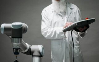 Scientist in a white lab coat uses a tablet to control a robotic arm in a lab setting with gray background