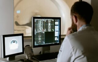 Radiologist studies MRI scans on a monitor in a clinical imaging room in front of a workstation.
