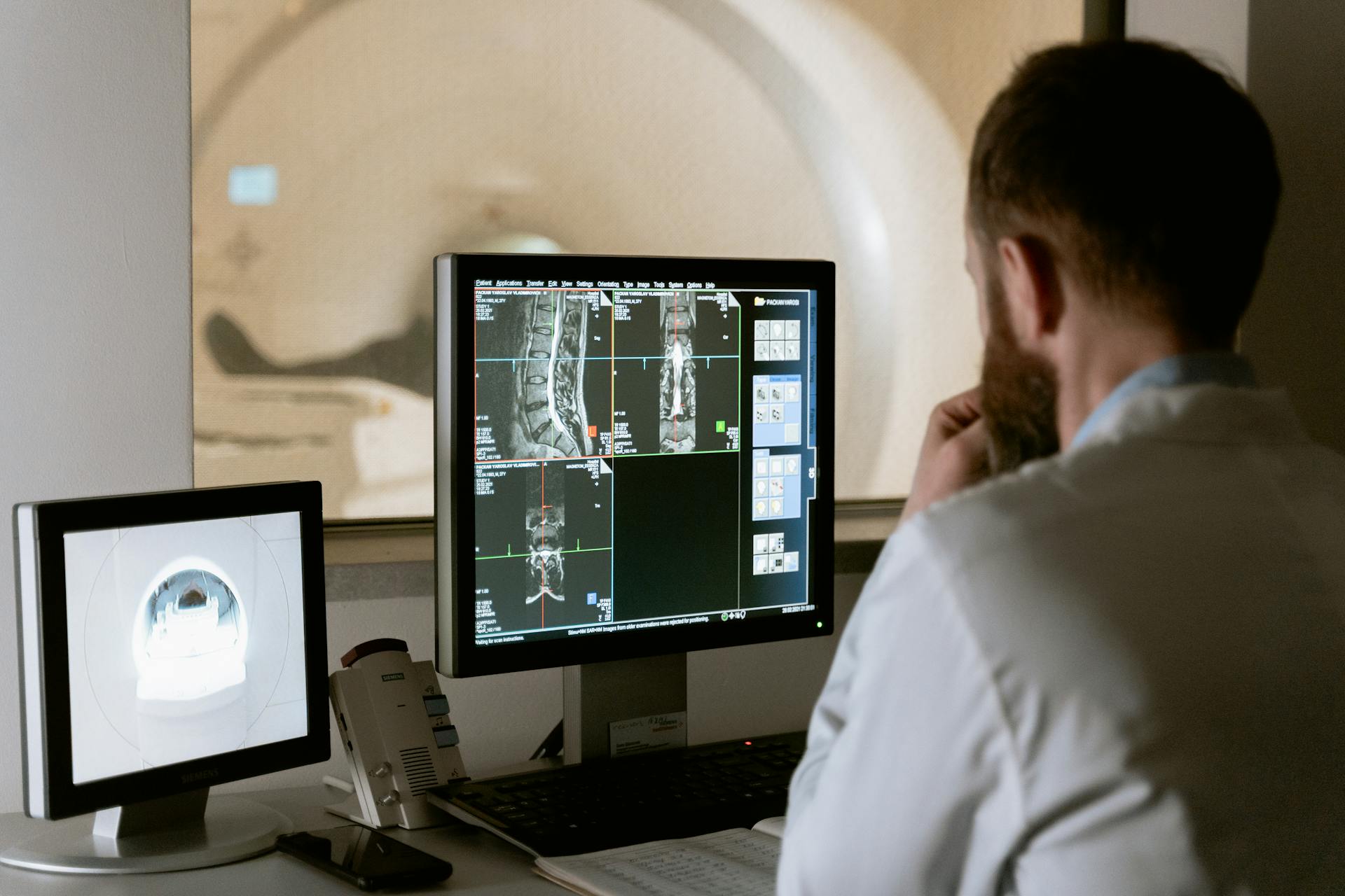 Radiologist studies MRI scans on a monitor in a clinical imaging room in front of a workstation.