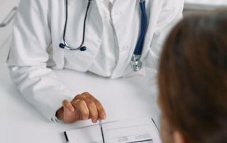 Female doctor in a white coat with a stethoscope reviews a color-coded medical chart with a patient nearby at a desk.