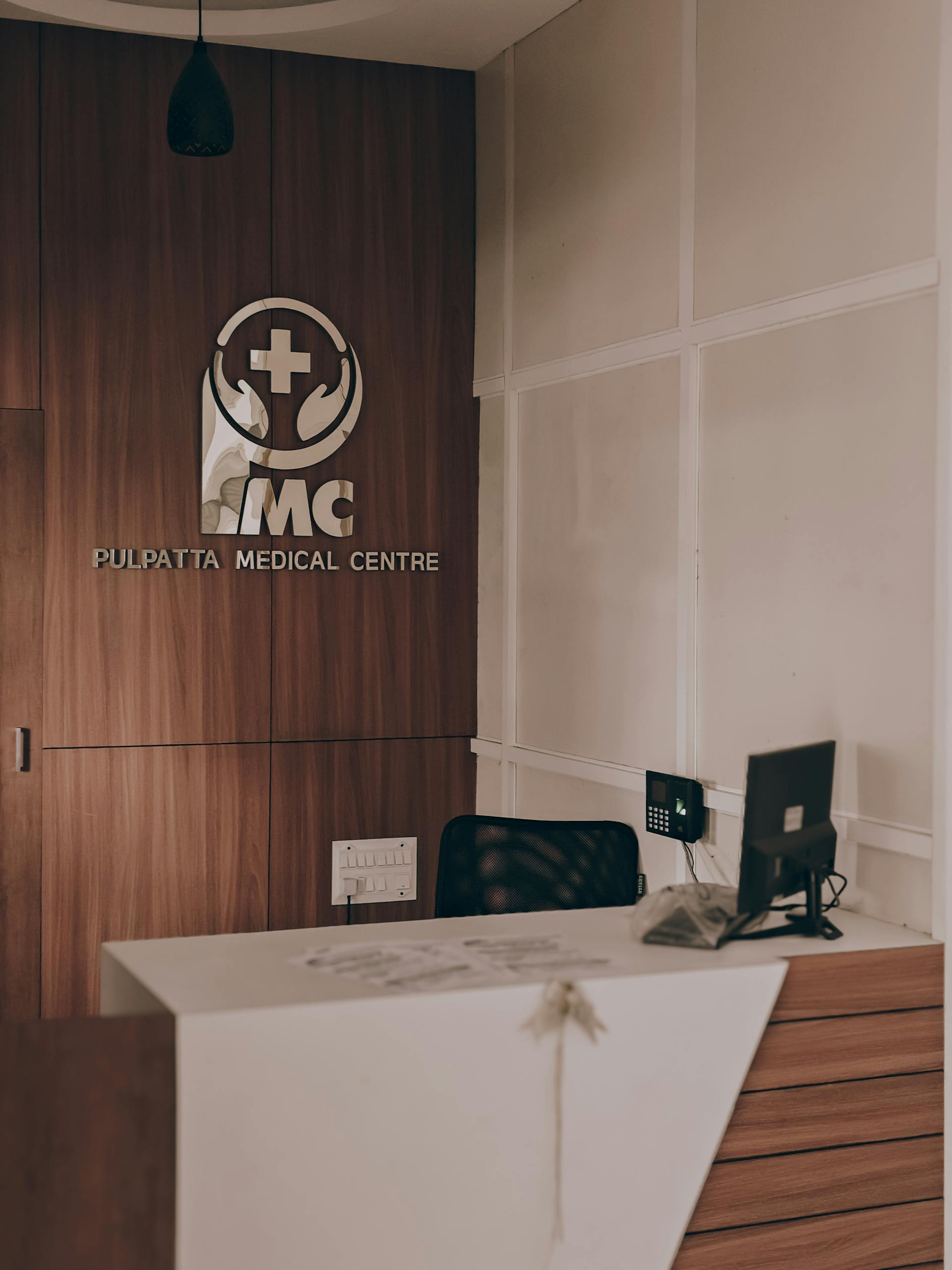 Reception desk at Pulpatta Medical Centre with the IMC logo on a wood-paneled wall.