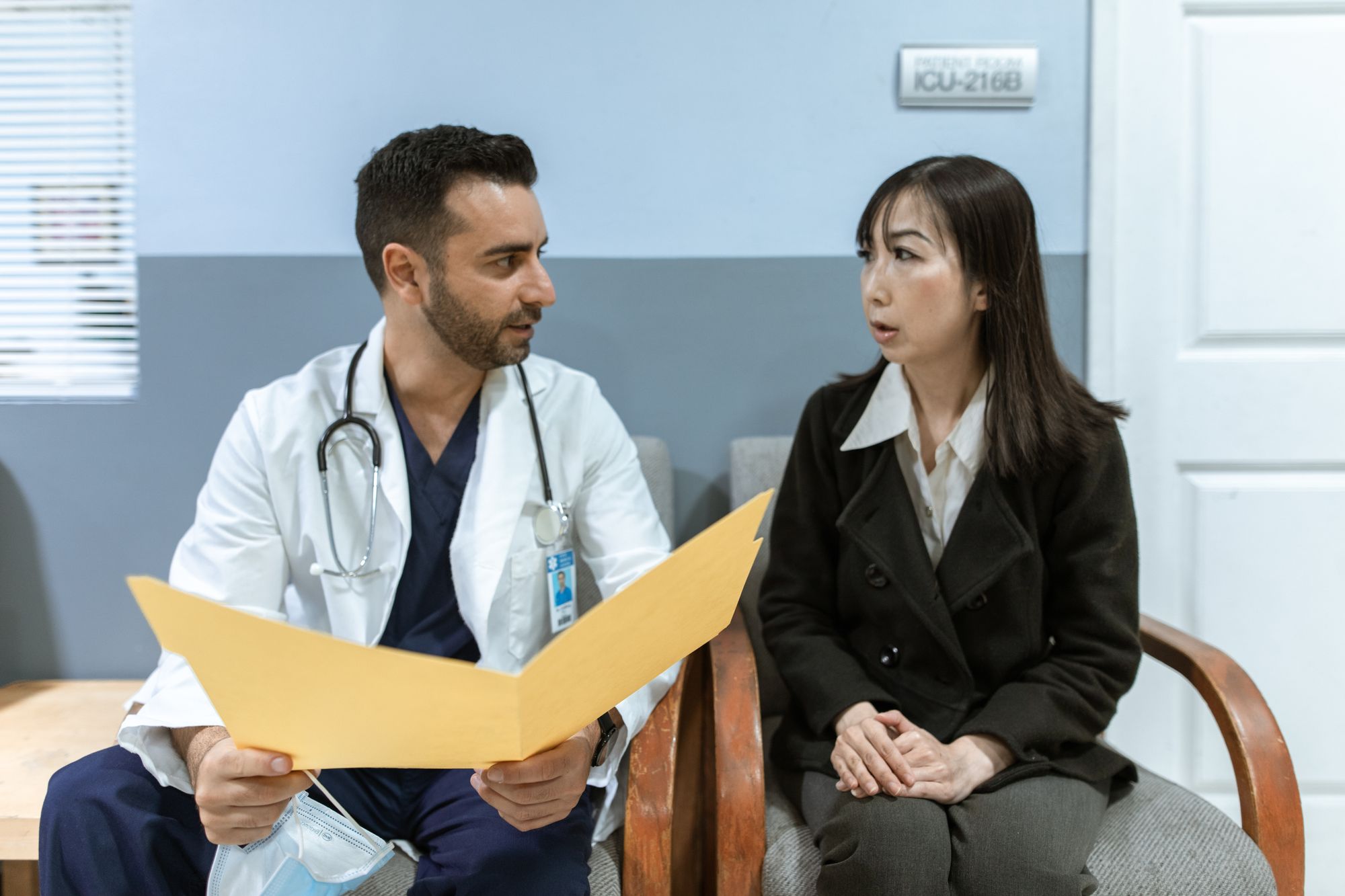 A clinician in a white coat explaining notes from a folder to a seated patient