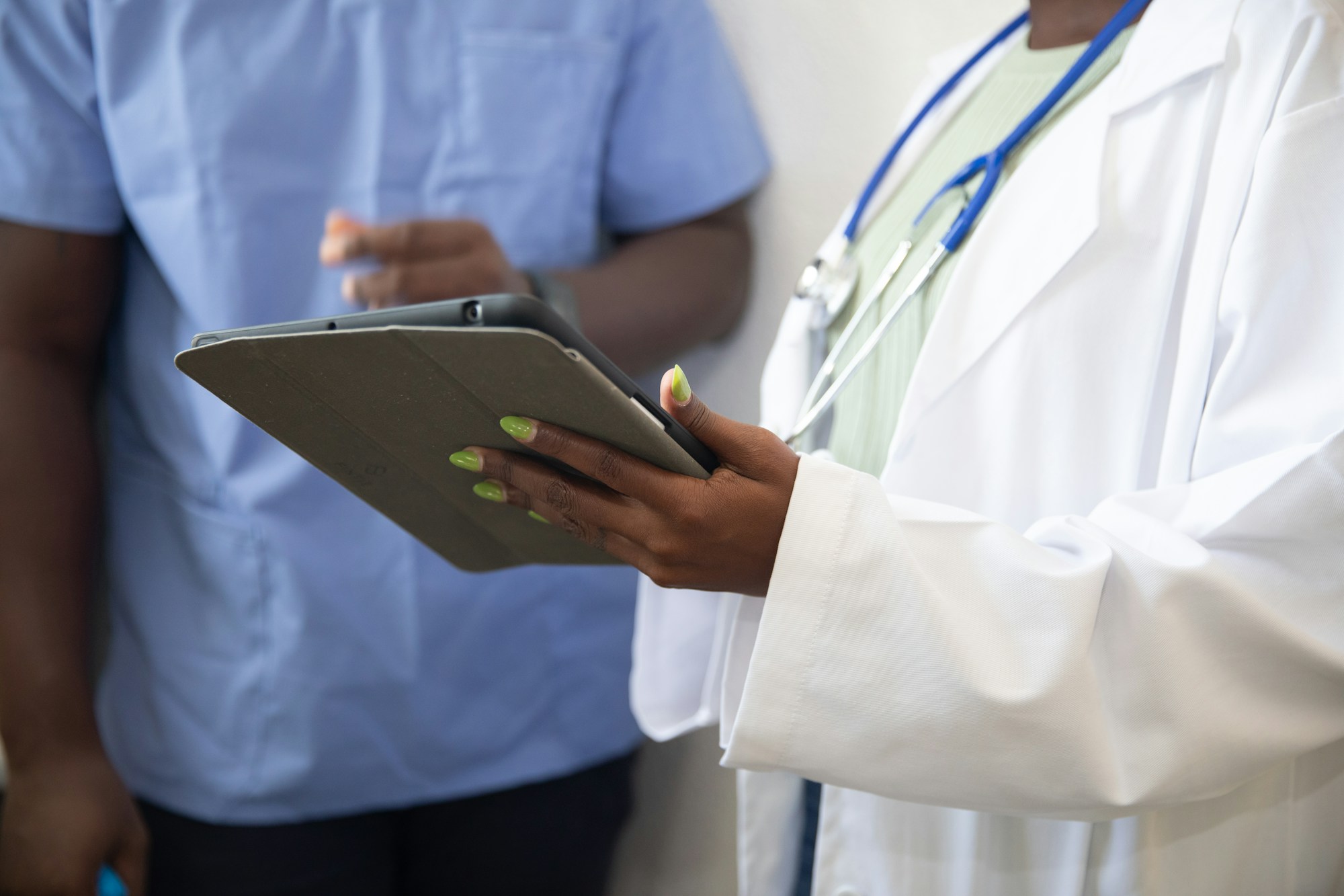 Clinician holding a tablet while talking with a colleague in scrubs inside a clinic
