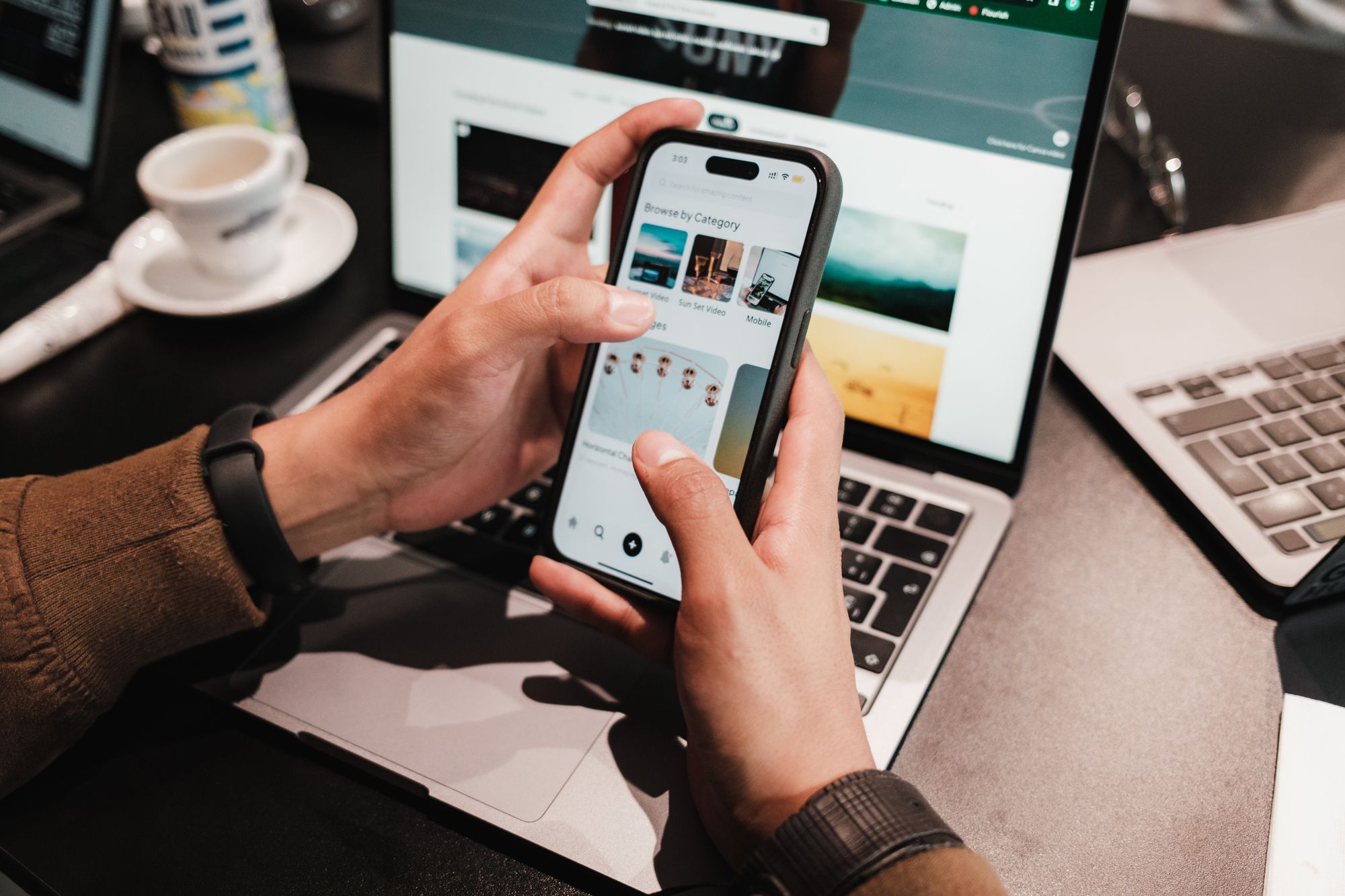Hands using a phone to browse a search screen with a laptop behind