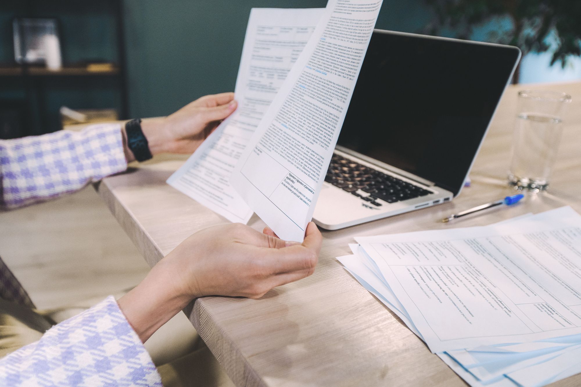 A person reading a printed statement at a desk beside a laptop