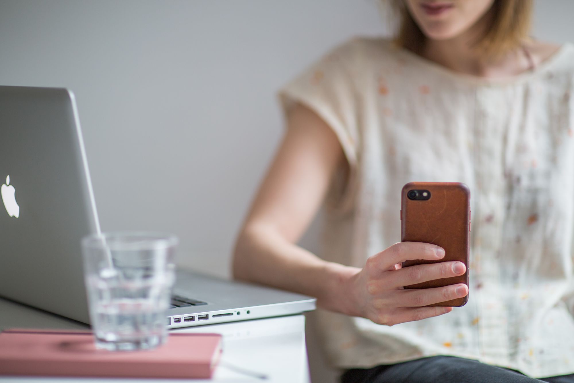 A person reading their phone at a desk beside a laptop