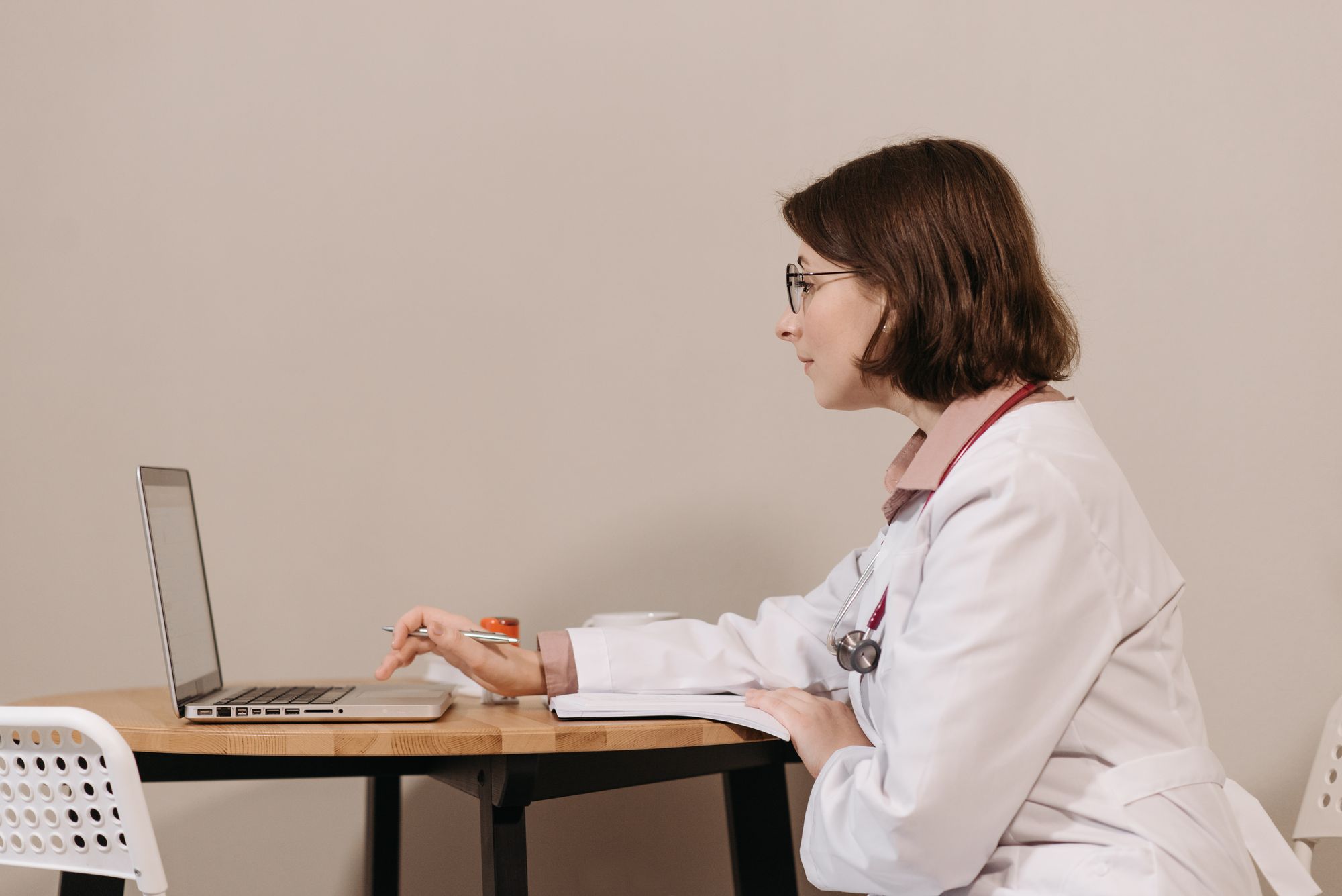 A physician in a white coat working at a laptop at a desk