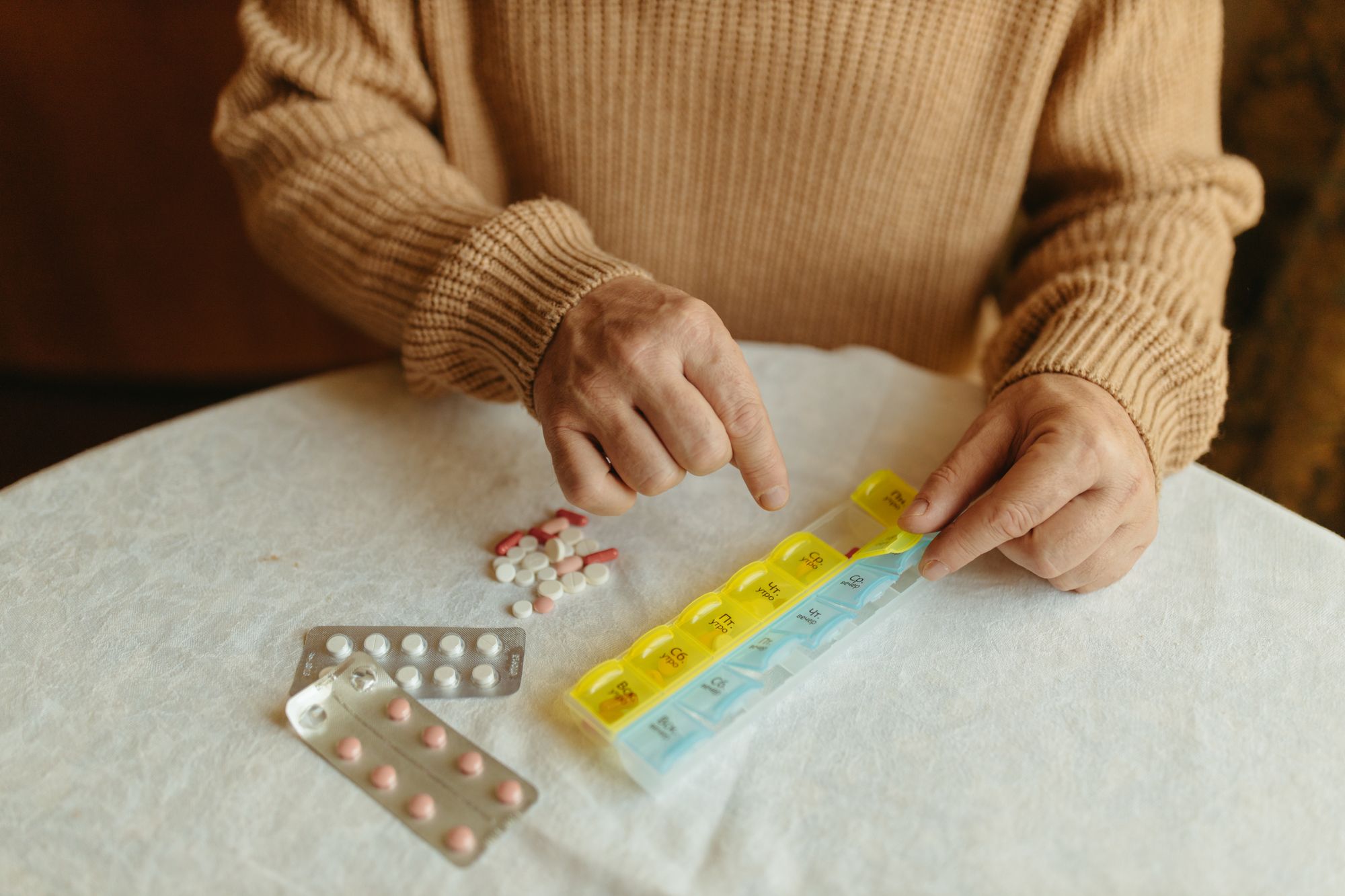 A person sorting daily medications into a weekly pill organizer