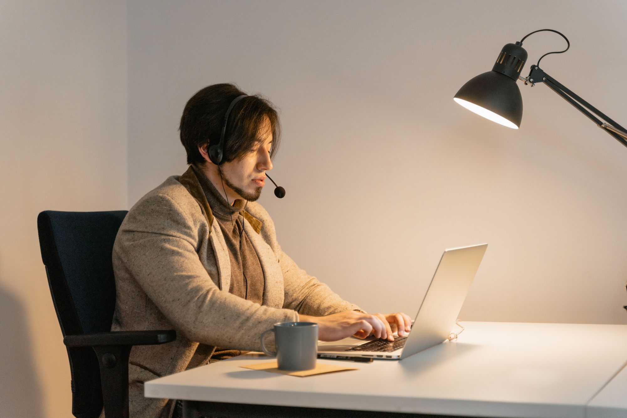 A person wearing a headset working at a laptop in a quiet home office