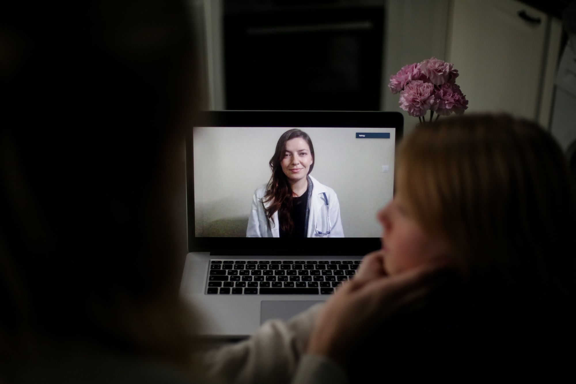 A patient on a video call with a clinician visible on the laptop screen