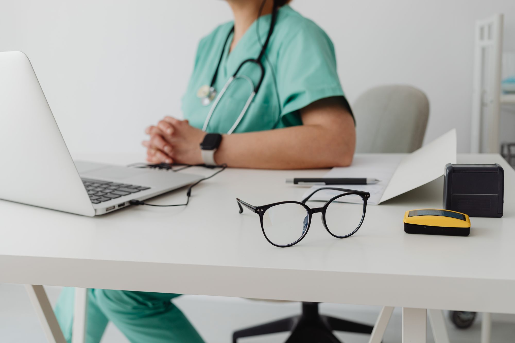 A healthcare professional in scrubs working at a laptop